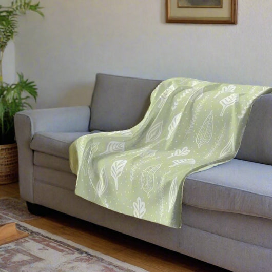 green and white throw blanket with white leaves on a grey sofa